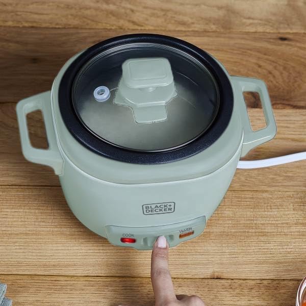 Green electric hot pot with a hand pressing a button on a wooden surface
