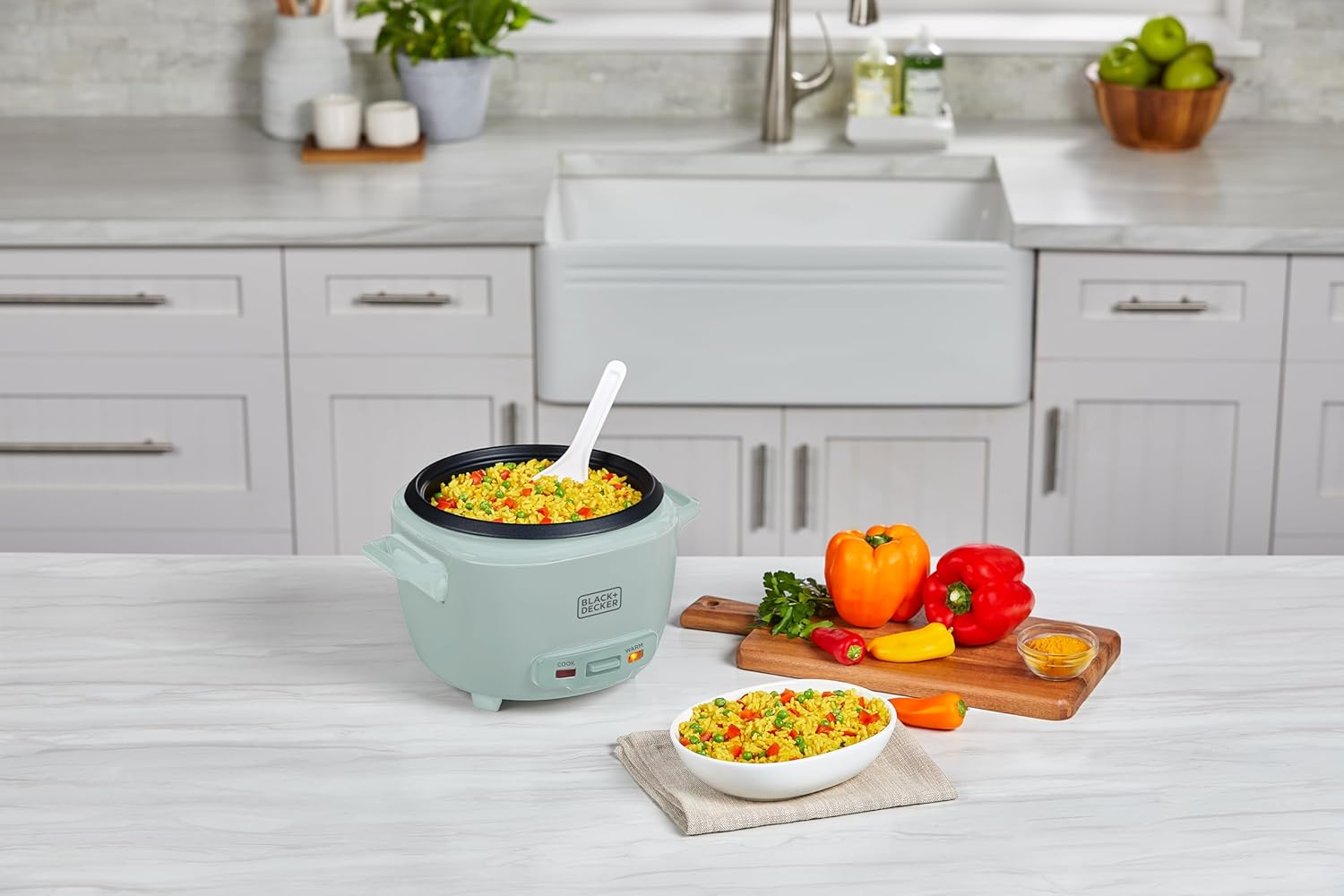Small rice cooker with food on a kitchen counter, surrounded by vegetables.