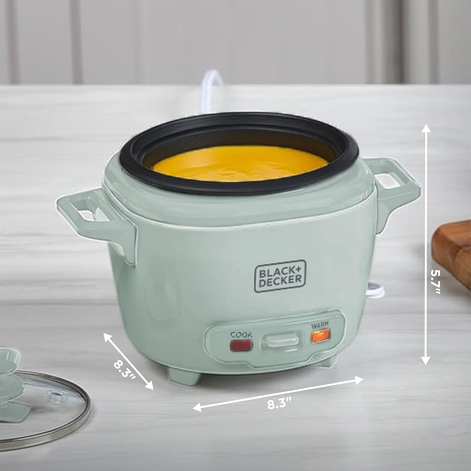 Green rice cooker with yellow contents on a white surface with dimensions, featuring Black+Decker branding.