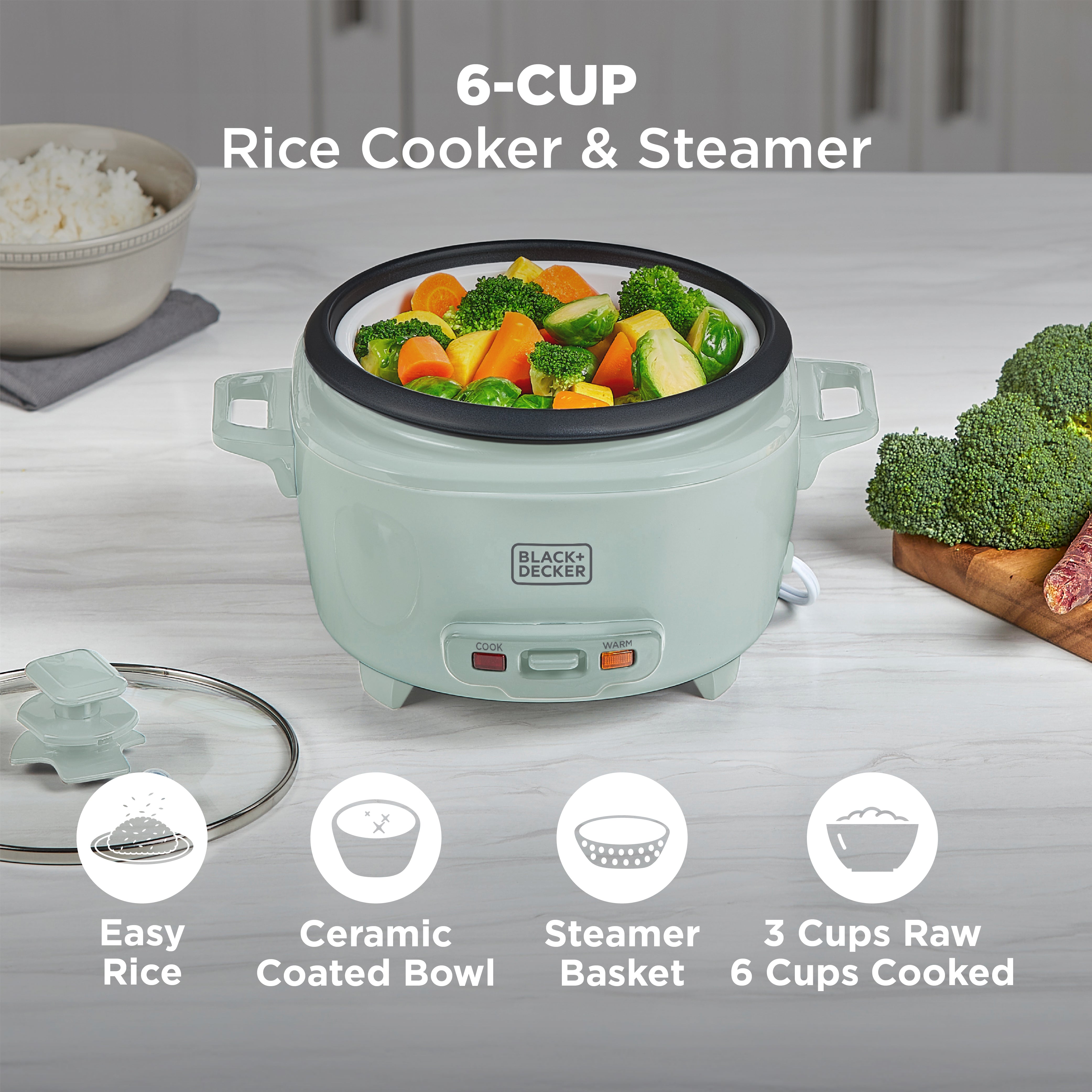 Mint green rice cooker with steamer basket containing vegetables on a light wooden surface.