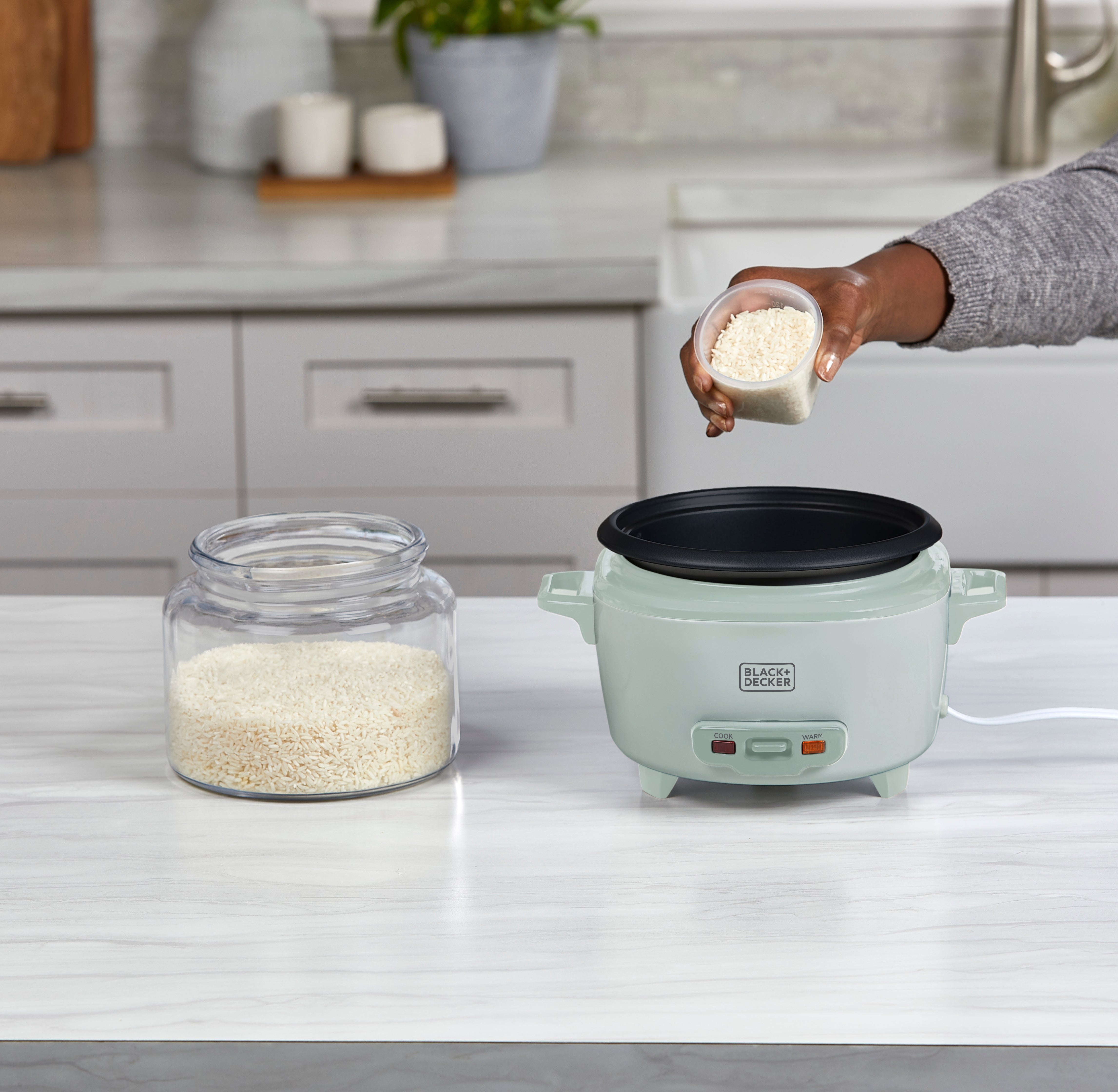 Person adding rice to a rice cooker on a kitchen counter