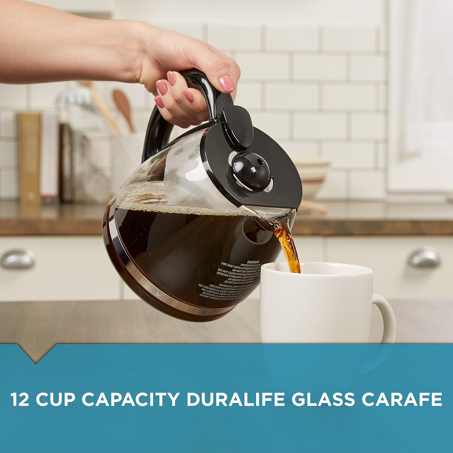 Person pouring coffee from a 12 cup capacity Duralife glass carafe into a white mug in a kitchen.