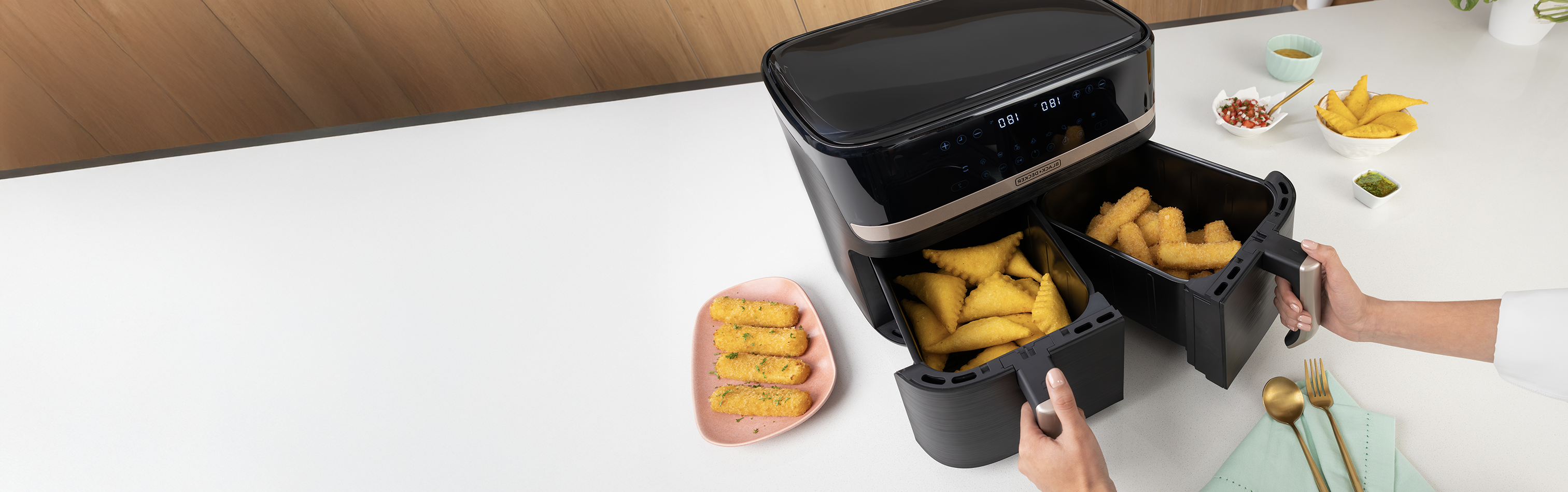Black air fryer on a white countertop with food items around