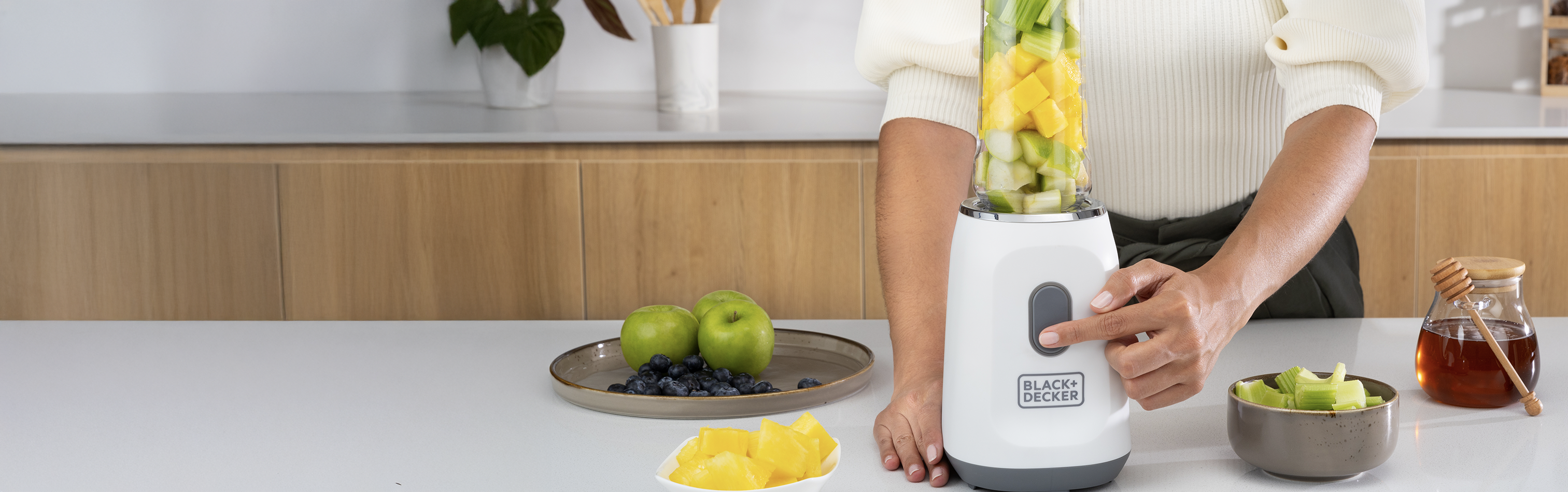 Person using a blender with fruits and vegetables on a kitchen counter