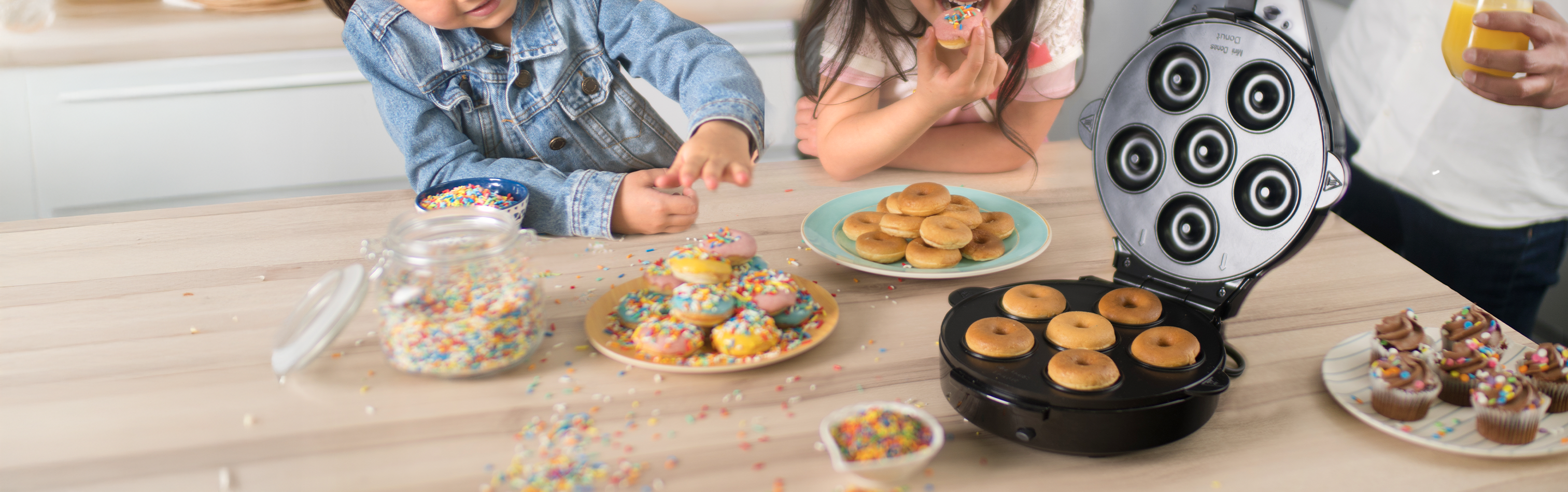 Children making donuts with a donut maker on a wooden table.