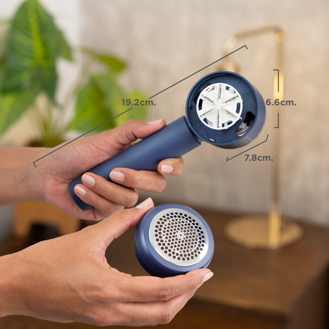 Blue handheld device held by hands with measurements indicated, blurred indoor background