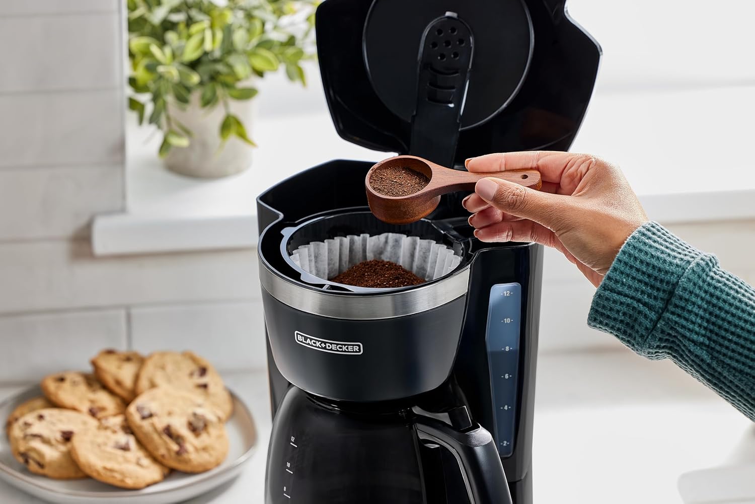 Person preparing coffee using a Black & Decker coffee maker with cookies on a plate in the background.