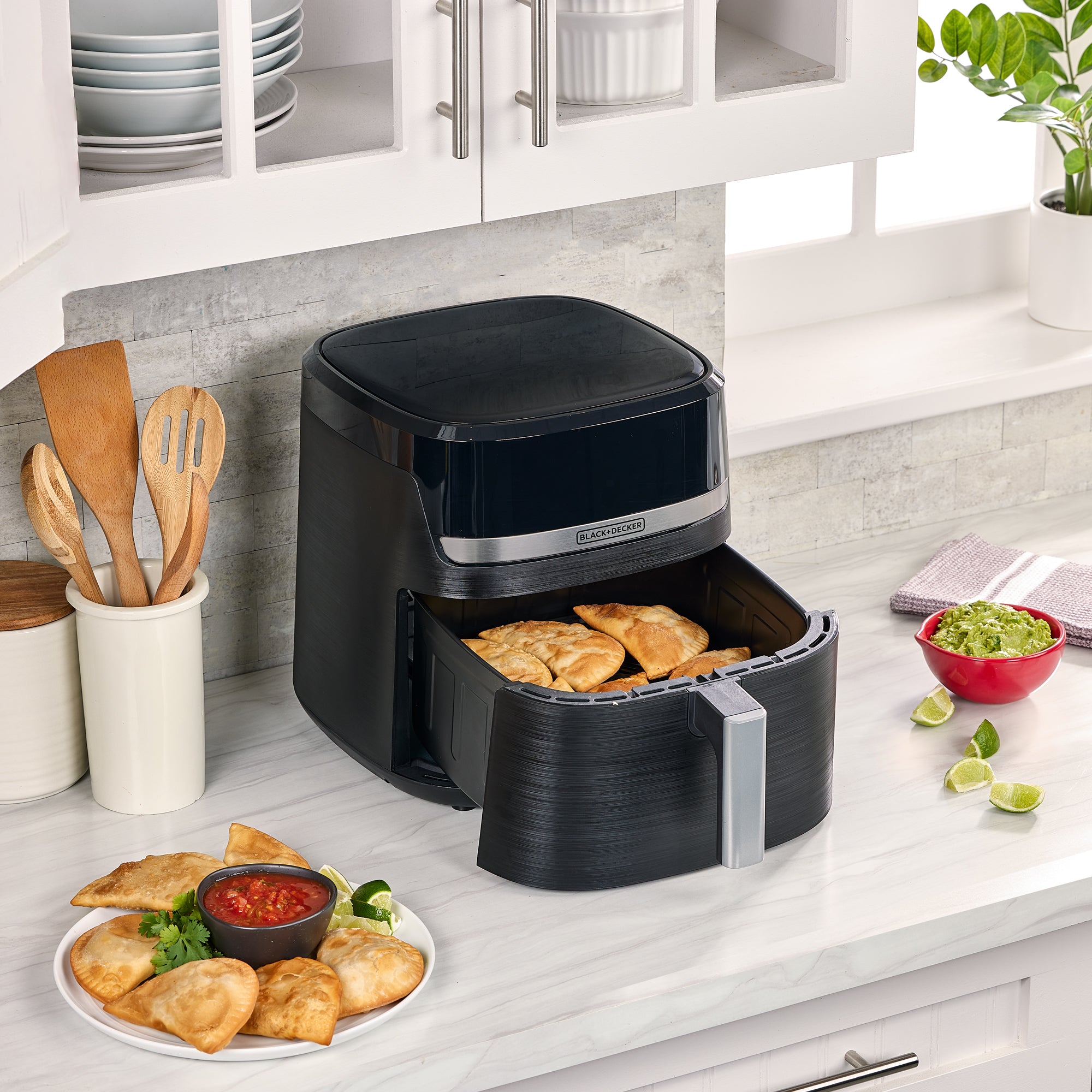 Black air fryer on a kitchen counter with food items around