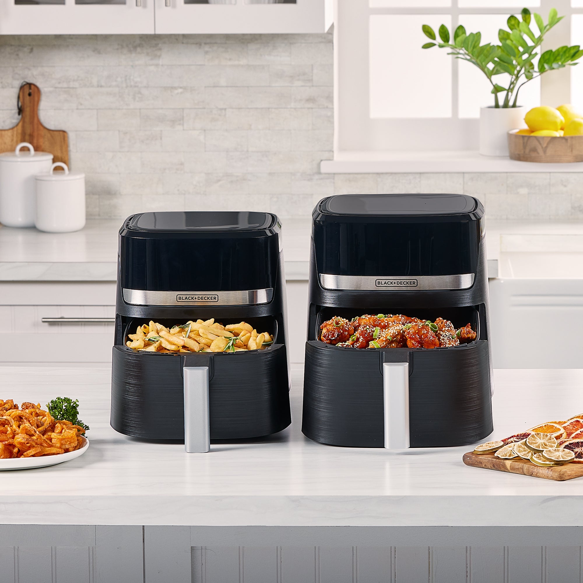 Two Black+Decker air fryers on a kitchen counter with food inside, surrounded by kitchen items.