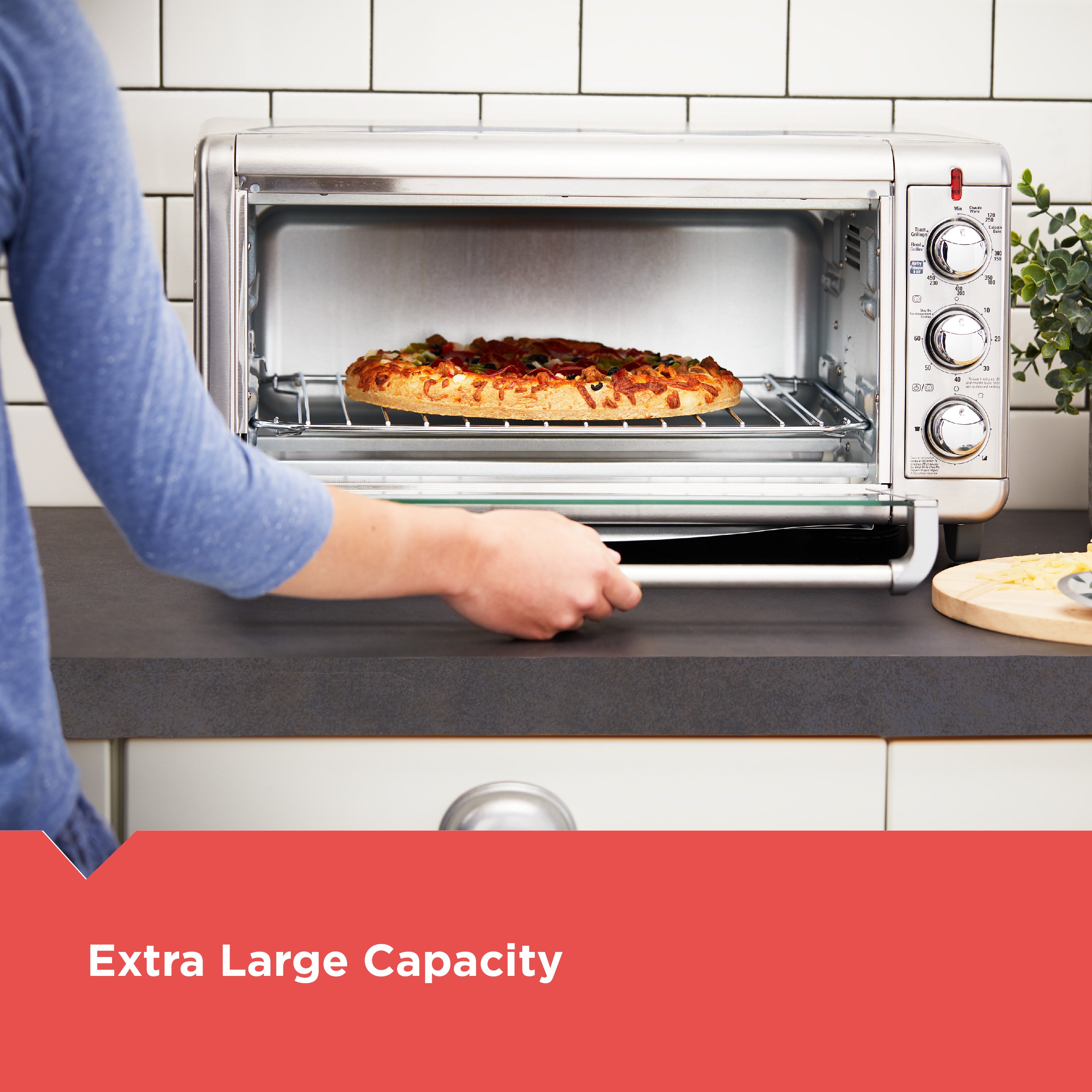 Person placing a pizza into a toaster oven with 'Extra Large Capacity' text.