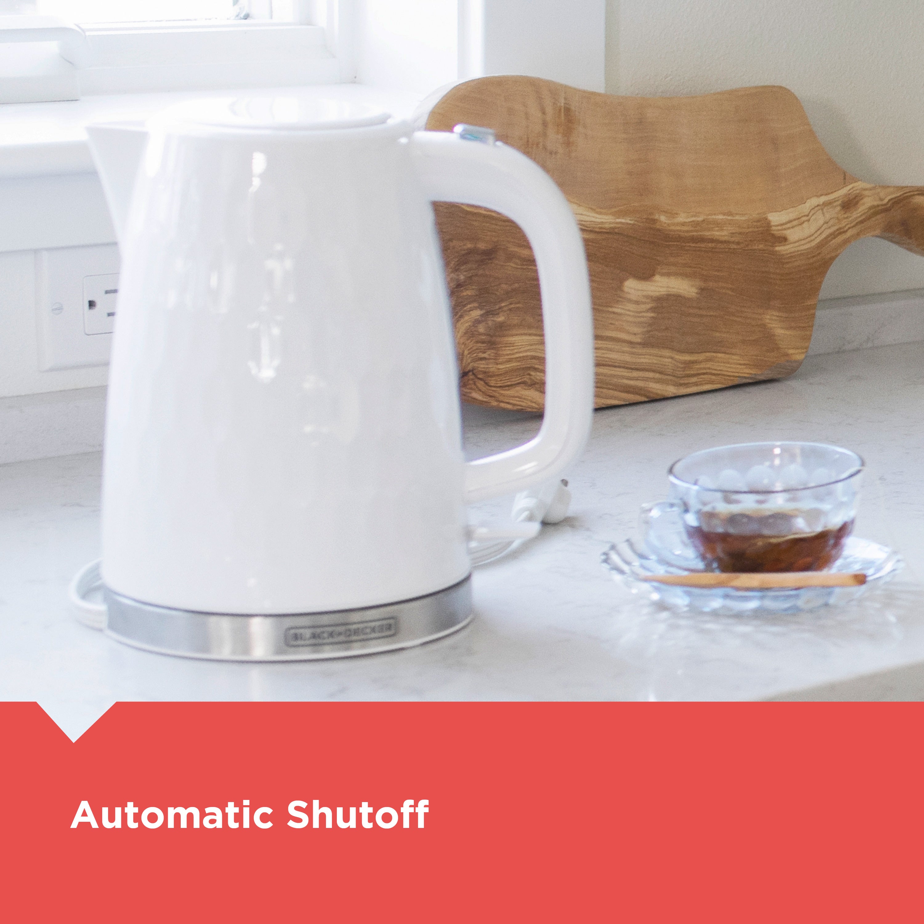 White electric kettle on a kitchen counter with a glass of tea and a wooden cutting board.