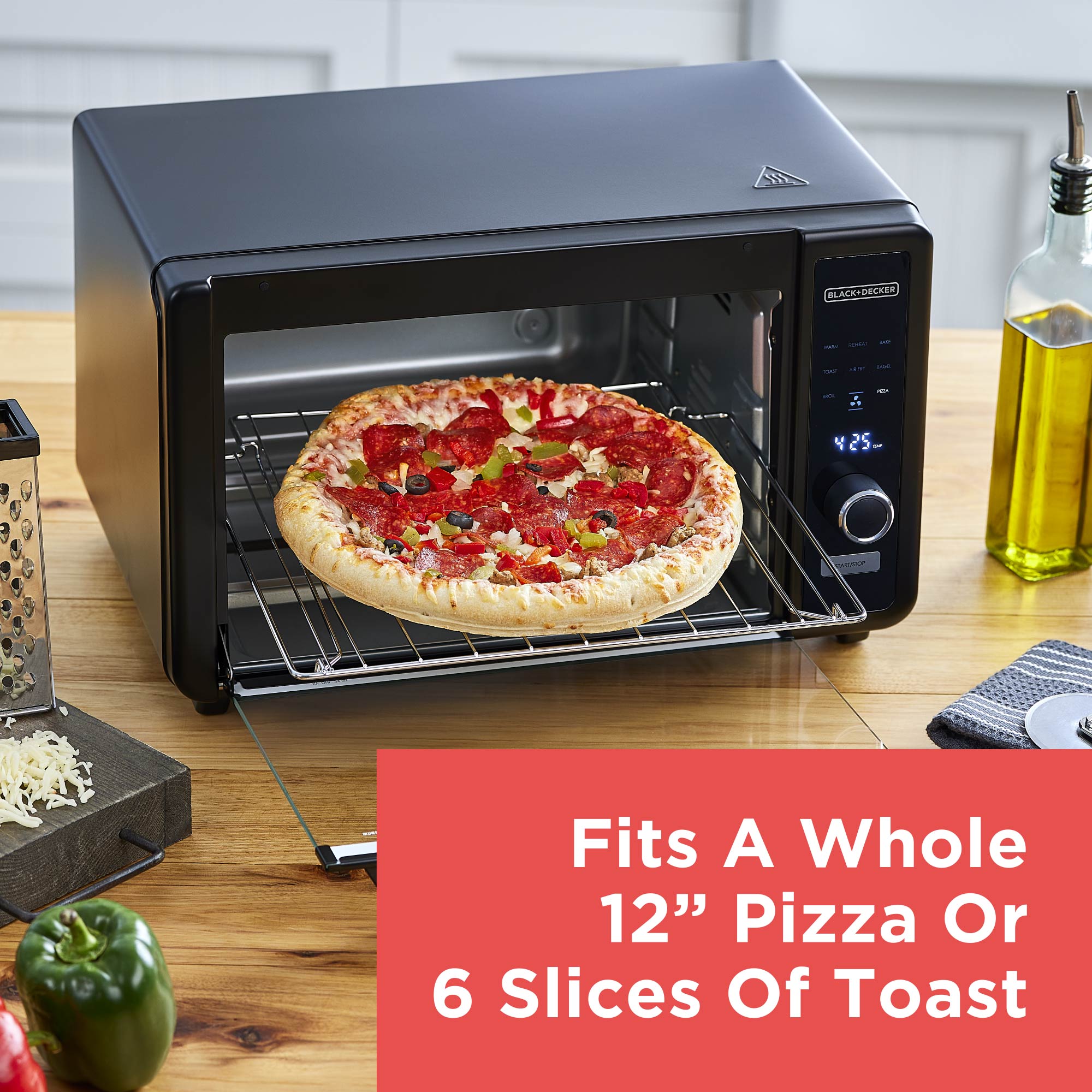 Black toaster oven with a pizza inside on a wooden countertop, with text about size capabilities.
