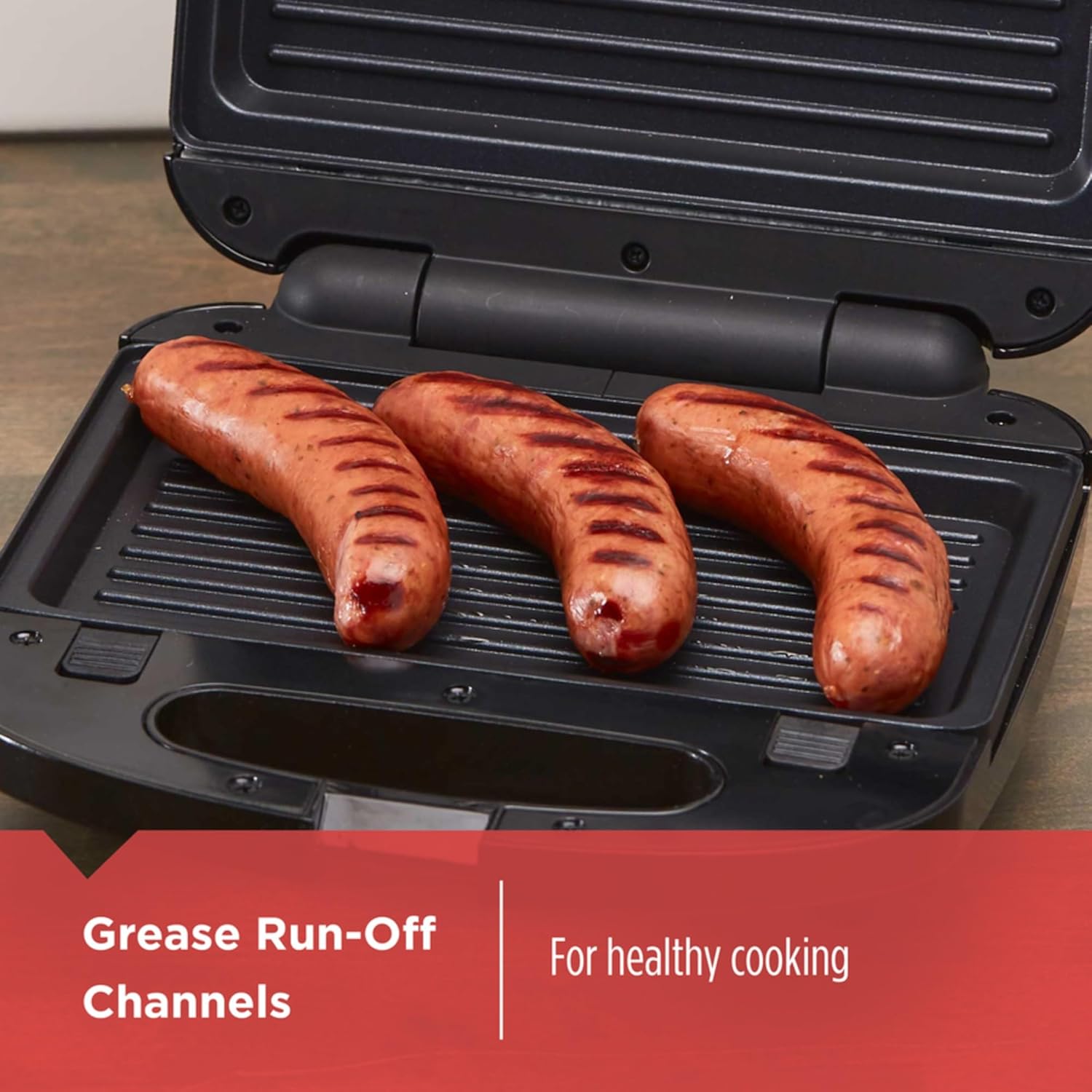 Three sausages cooking on a black grill with text about grease run-off channels.