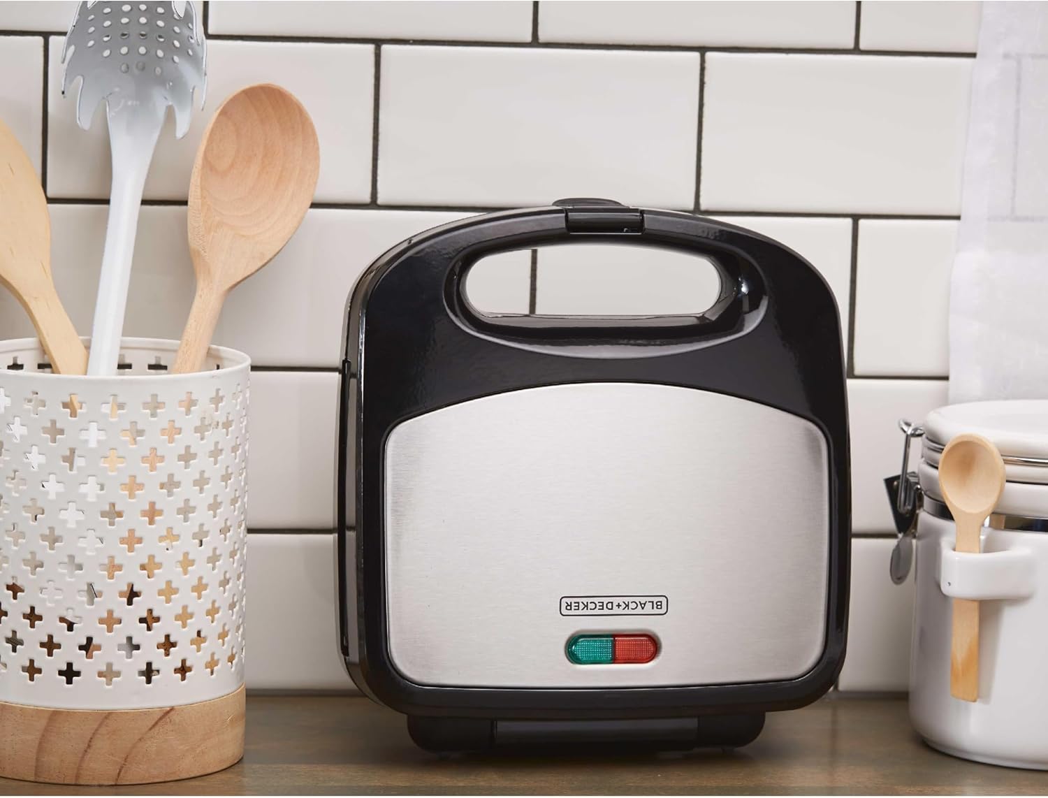 Black and silver waffle amker on a kitchen counter with tiled wall in the background