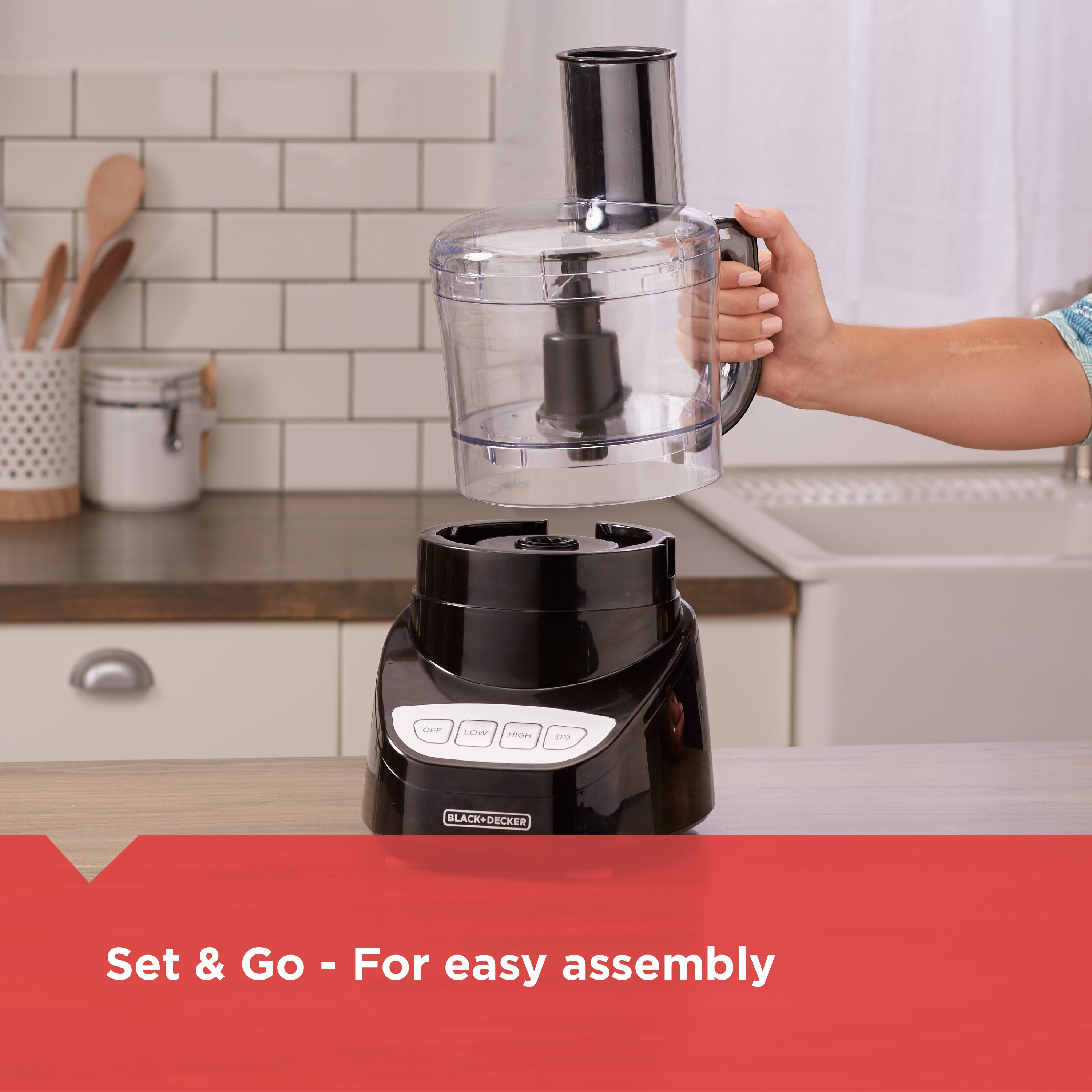 Black food processor with a person holding its container in a kitchen setting.