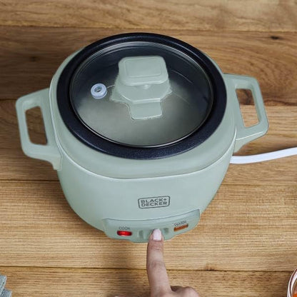 Green electric hot pot with a hand pressing a button on a wooden surface