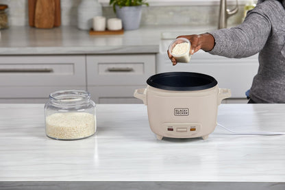 Person adding rice to a Black & Decker rice cooker on a kitchen counter.