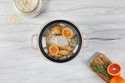 Cooking pot with food on a light gray surface, surrounded by oranges and oats.