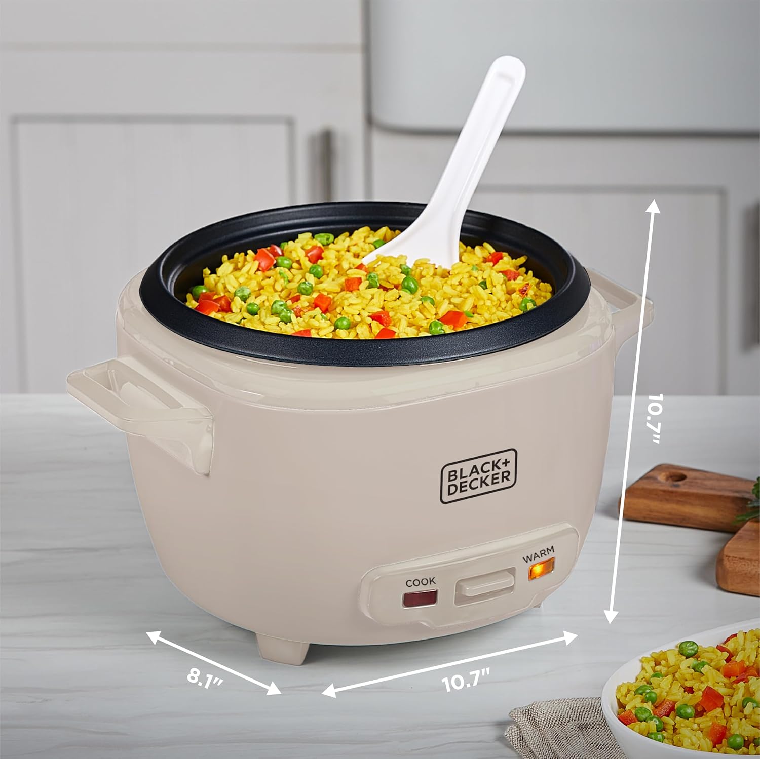 Black & Decker rice cooker with cooked vegetables and a spoon on a kitchen counter.