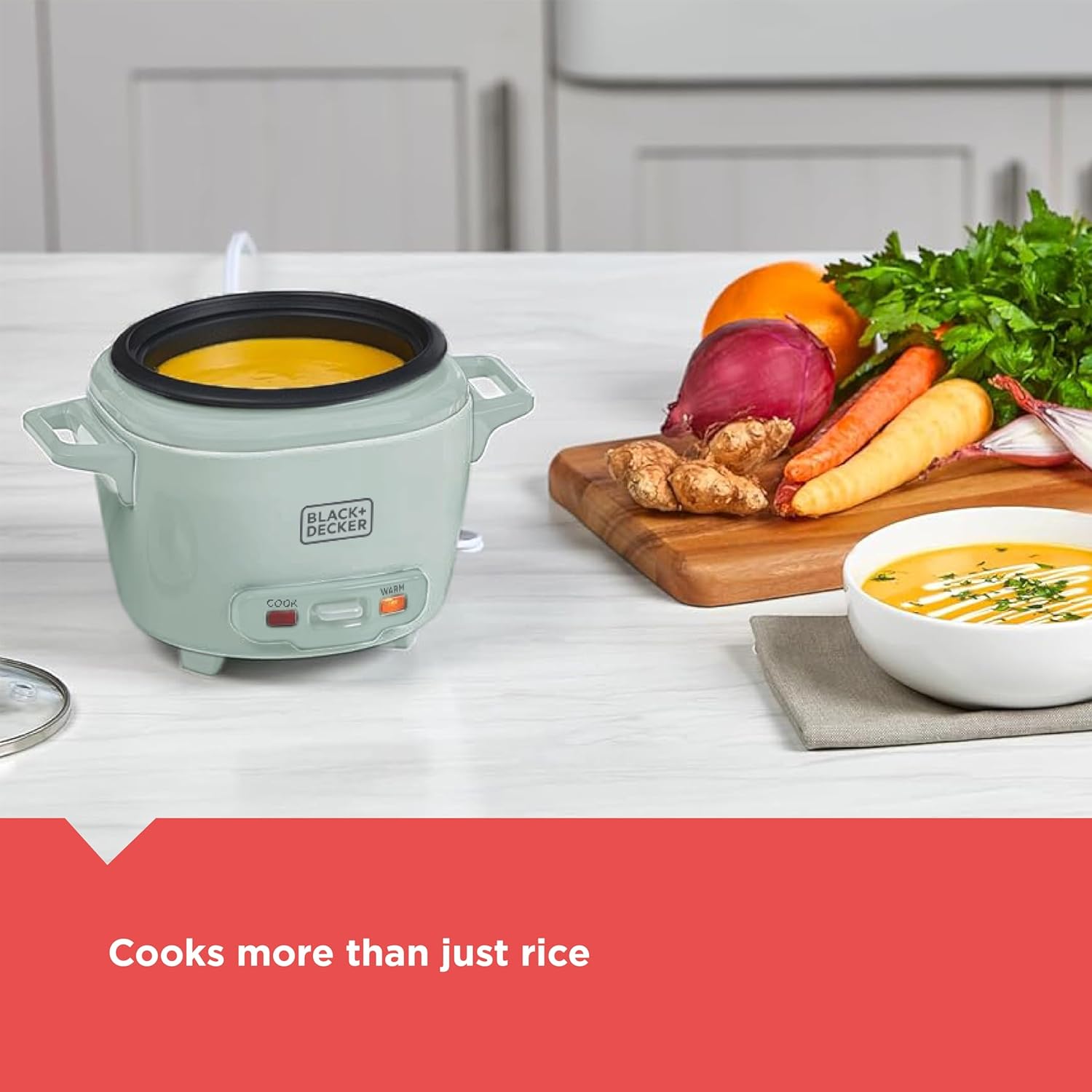 Small rice cooker on a kitchen counter with vegetables and a bowl of soup, featuring the Black+Decker brand.
