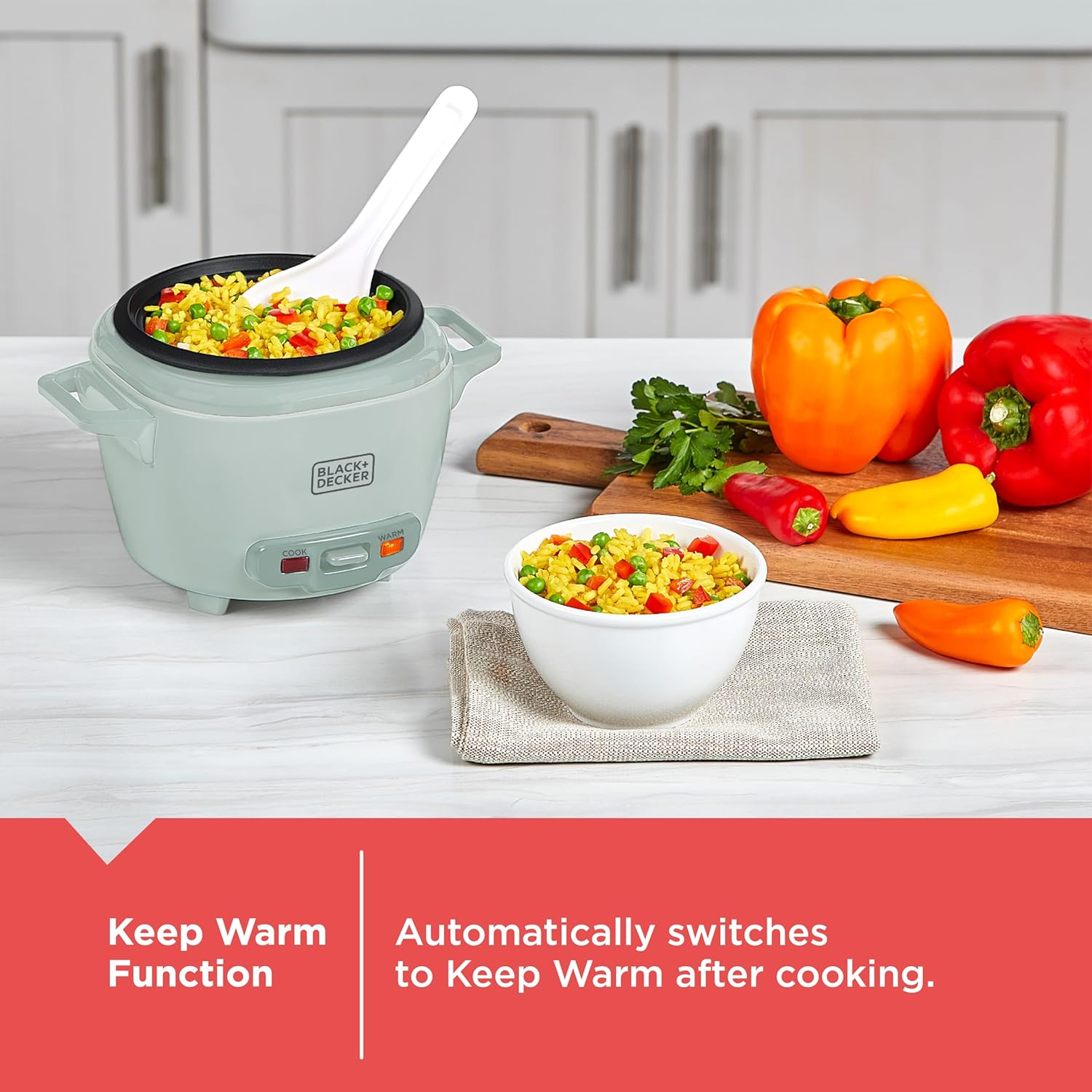 Green rice cooker with cooked vegetables, a bowl of rice, and colorful peppers on a kitchen counter.