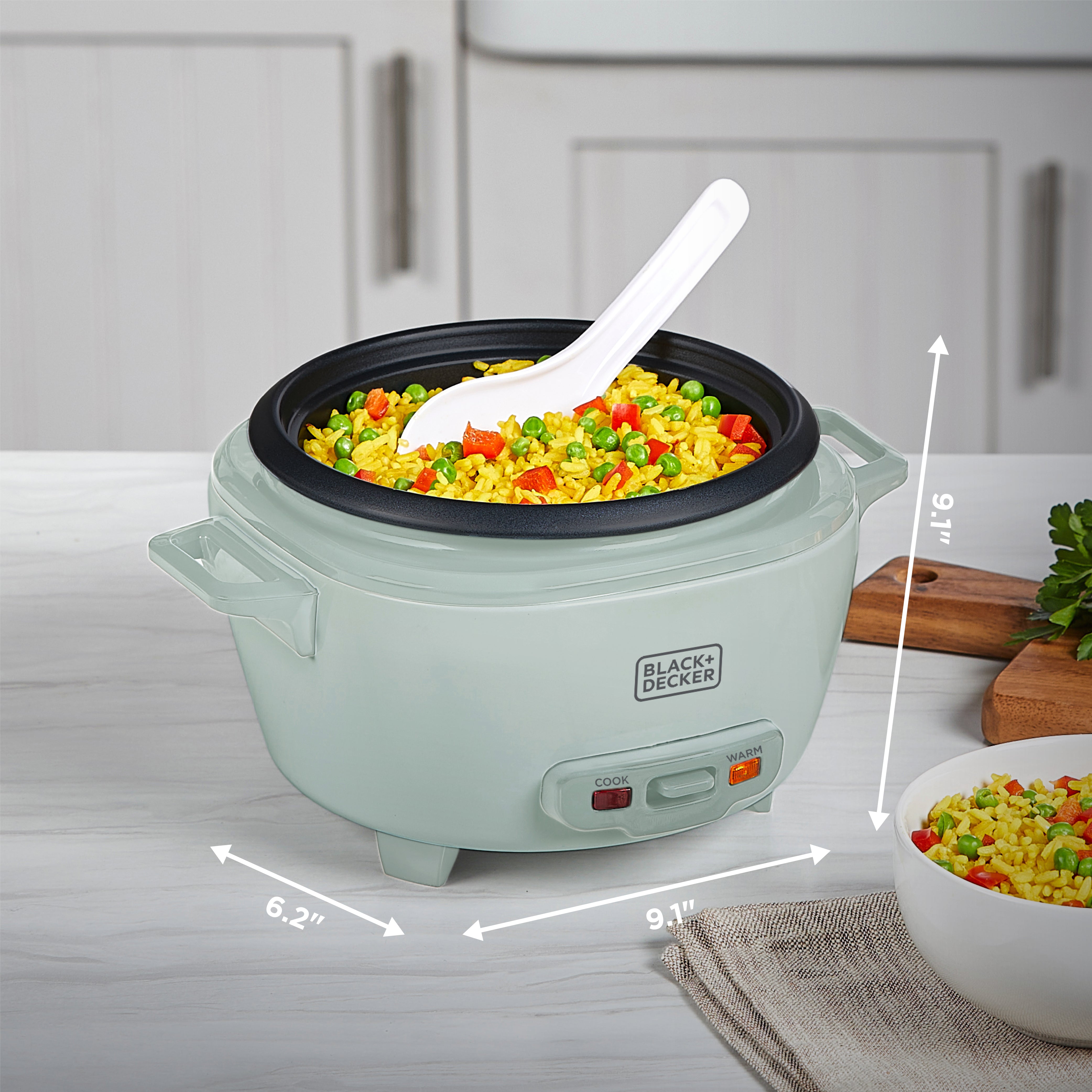 Green rice cooker with food inside on a kitchen counter, showing dimensions.