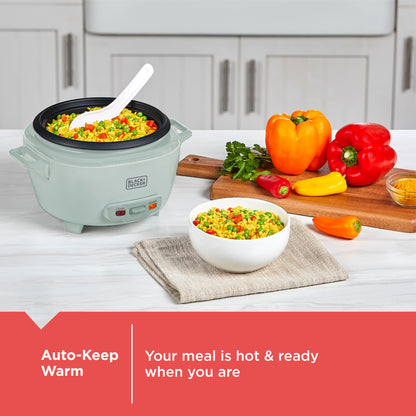 Green rice cooker with a bowl of rice and vegetables on a kitchen counter, surrounded by fresh peppers.