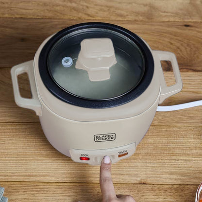 Black+Decker electric hot pot on a wooden surface with a hand pressing the power button.