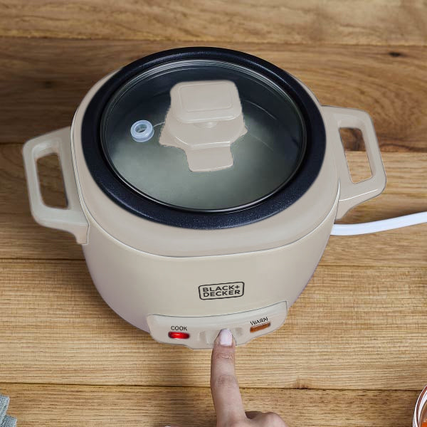 Black+Decker electric hot pot on a wooden surface with a hand pressing the power button.