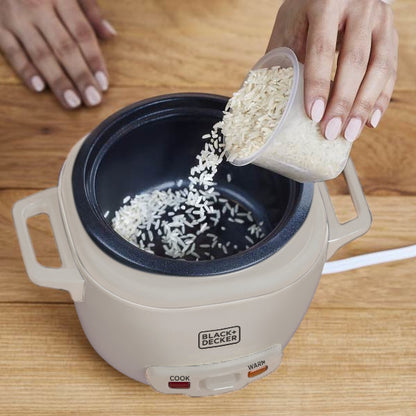 Person pouring rice into a Black+Decker electric rice cooker on a wooden surface