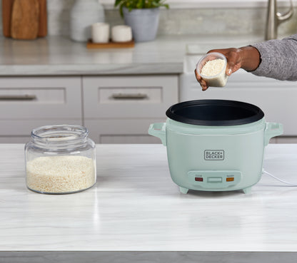 Person adding rice to a green rice cooker on a kitchen counter.