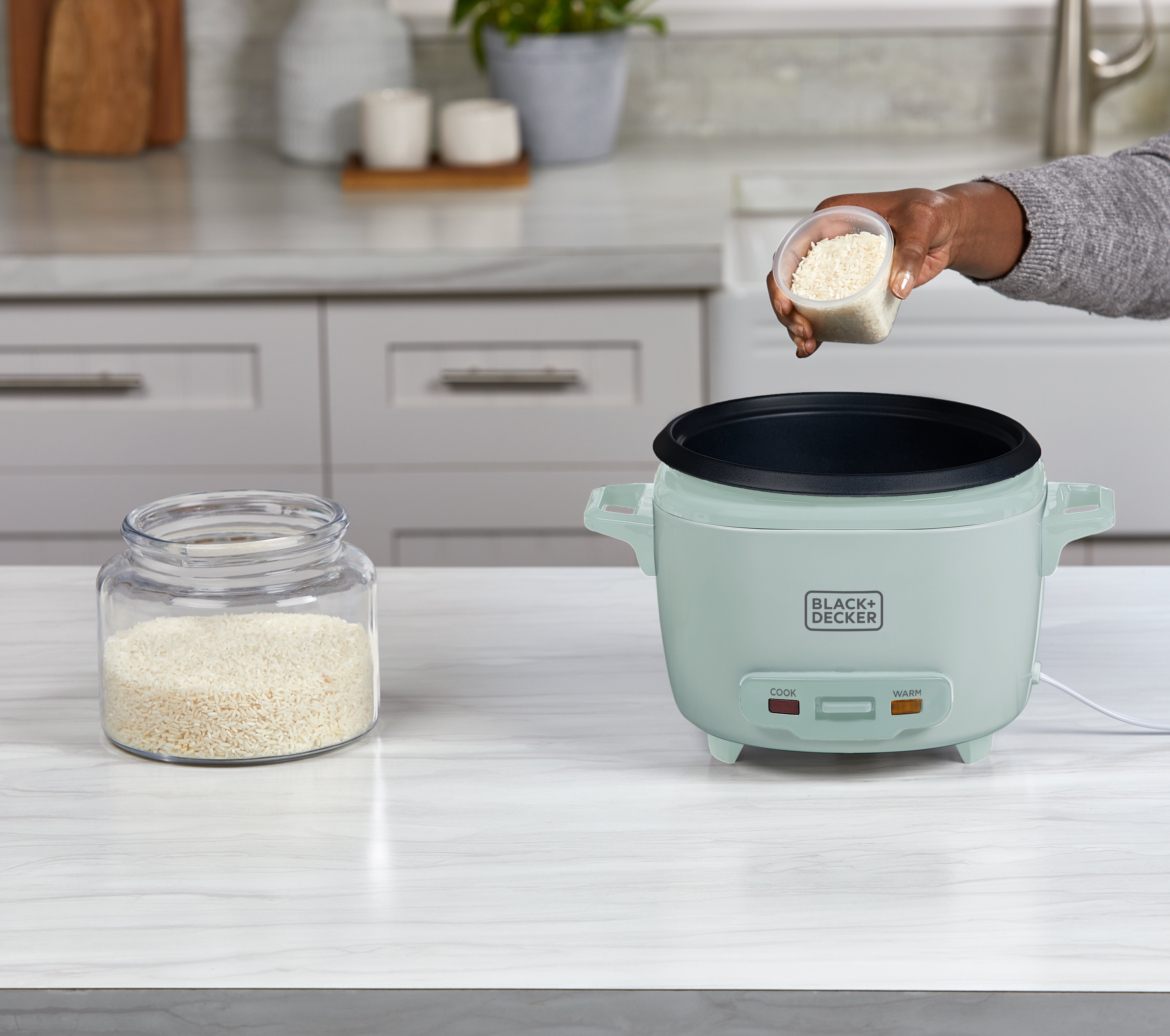 Person adding rice to a green rice cooker on a kitchen counter.