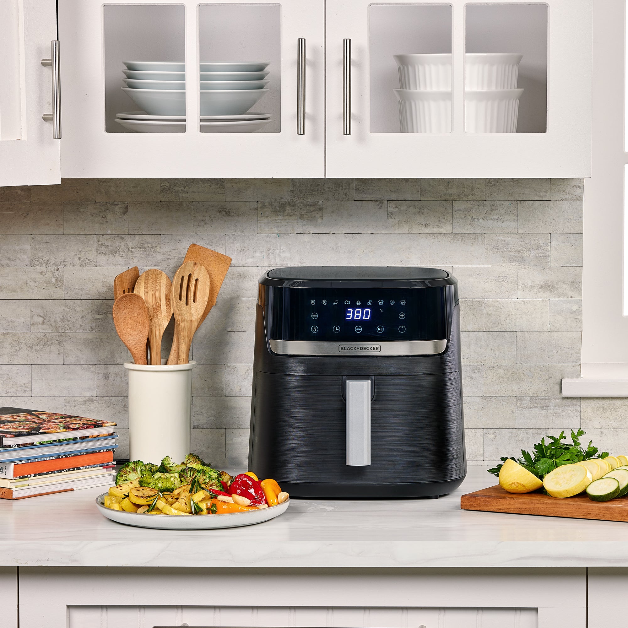 Black air fryer on a kitchen counter with vegetables and cookbooks in the background