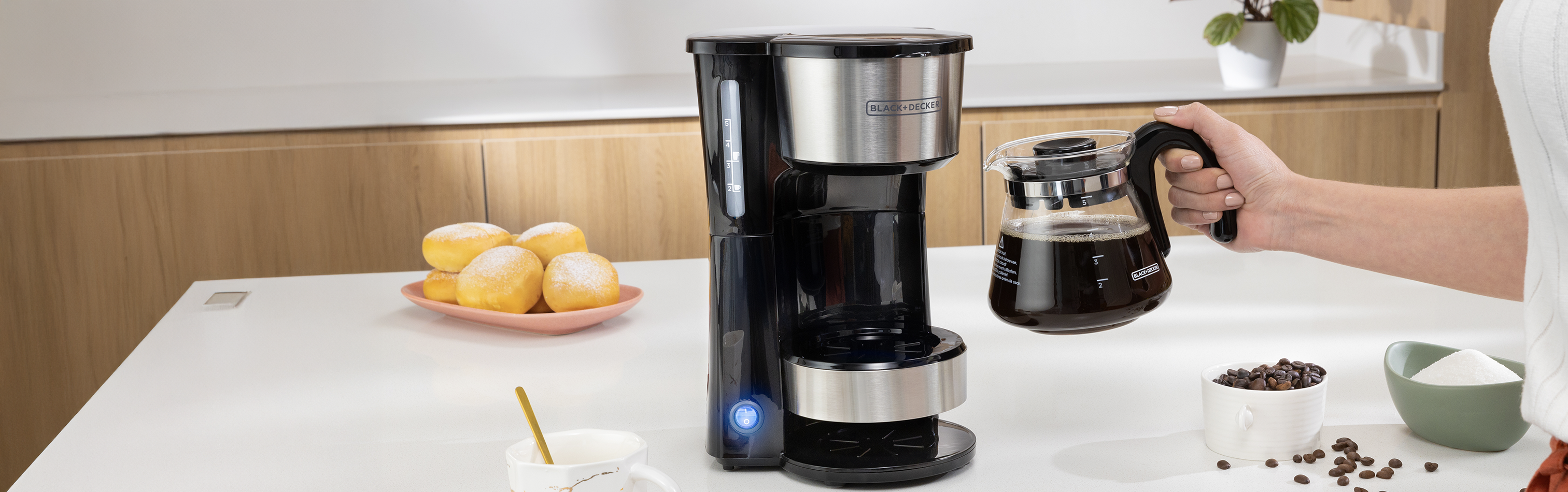 Person using a coffee maker on a kitchen counter with various items around