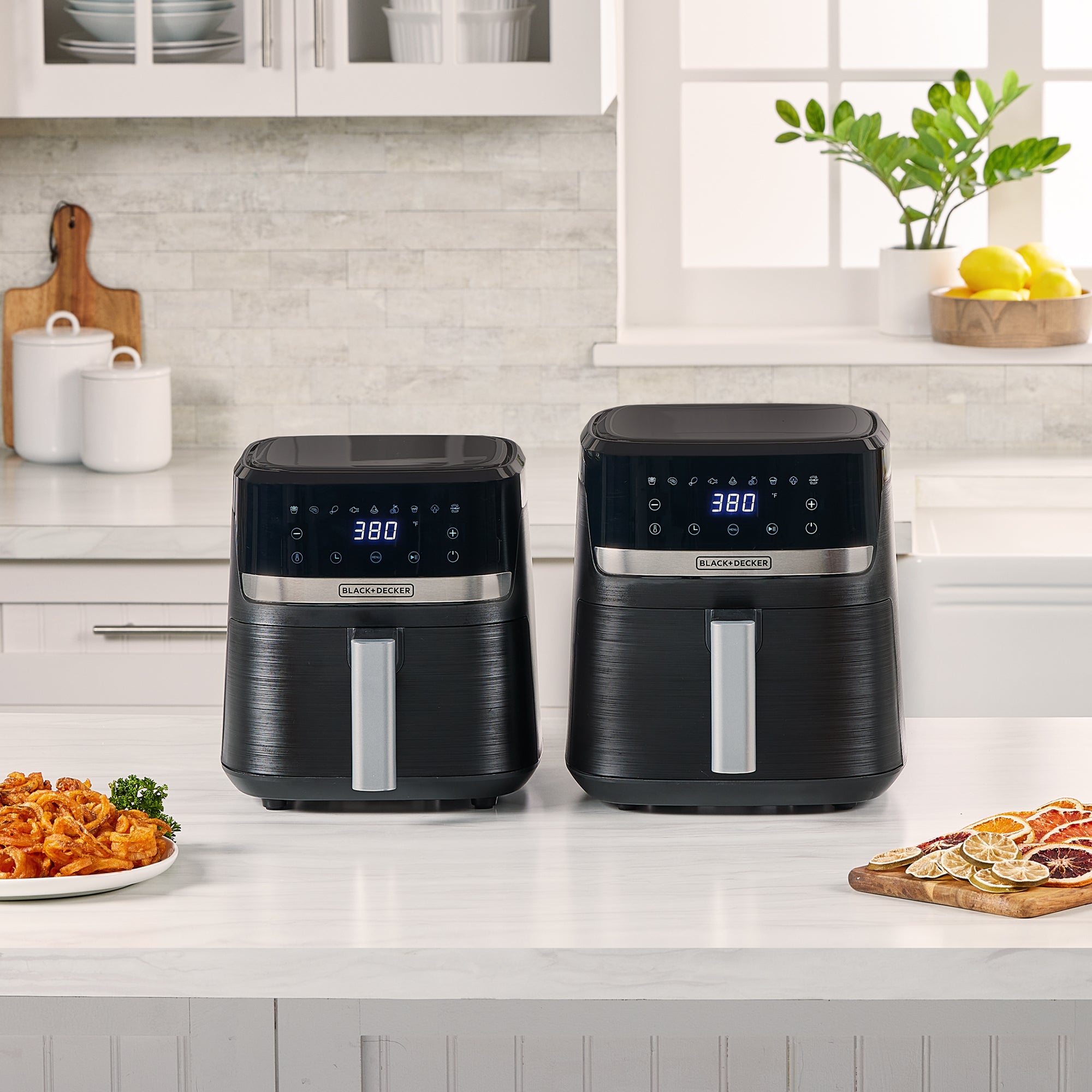Two black air fryers on a kitchen counter with food items around.