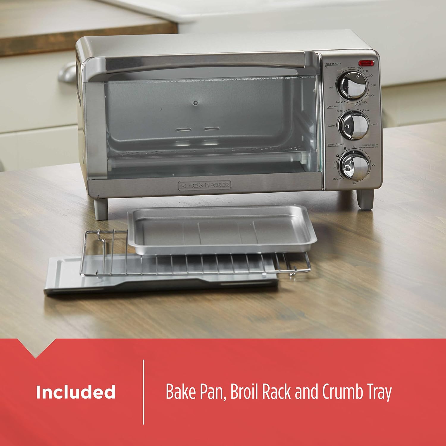 Silver toaster oven with included bake pan, broil rack, and crumb tray on a wooden surface.