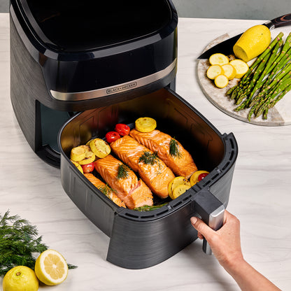 Black air fryer with salmon and vegetables on a white surface