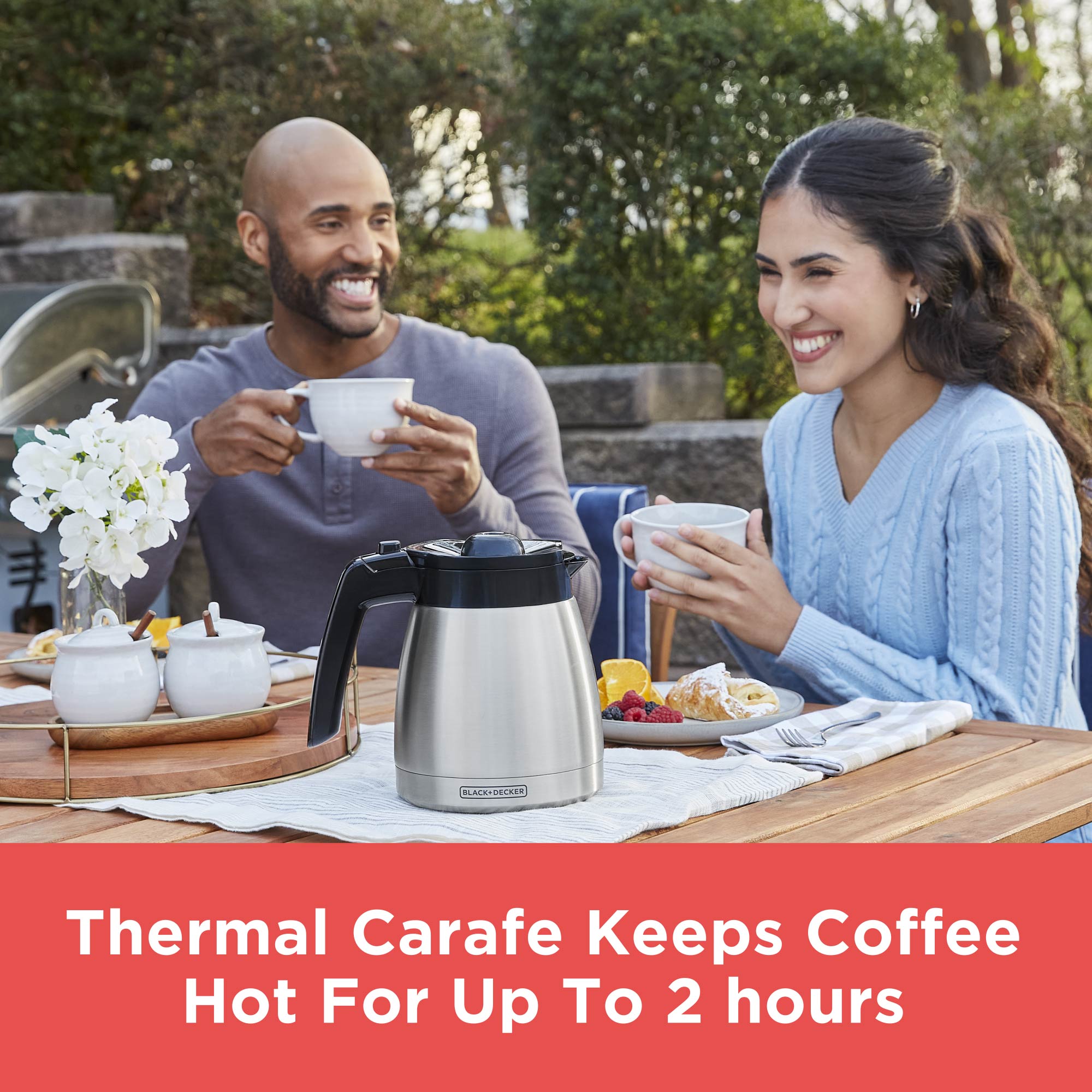 Man and woman enjoying coffee outdoors with a thermal carafe in the foreground.