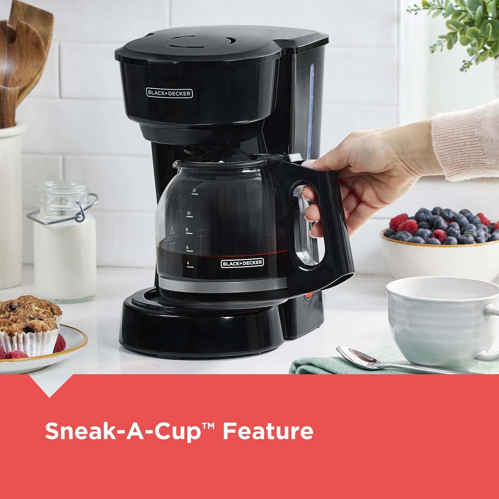 Black and Decker coffee maker with a hand holding it, on a kitchen counter with food items.