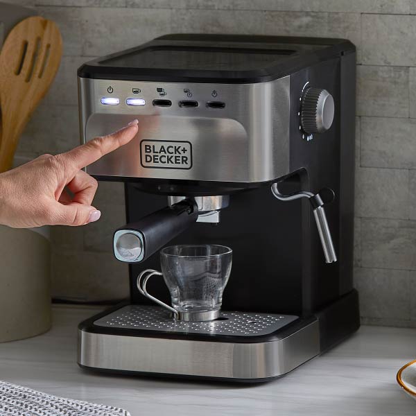 Black+Decker espresso machine with a hand pressing a button, set against a kitchen background.