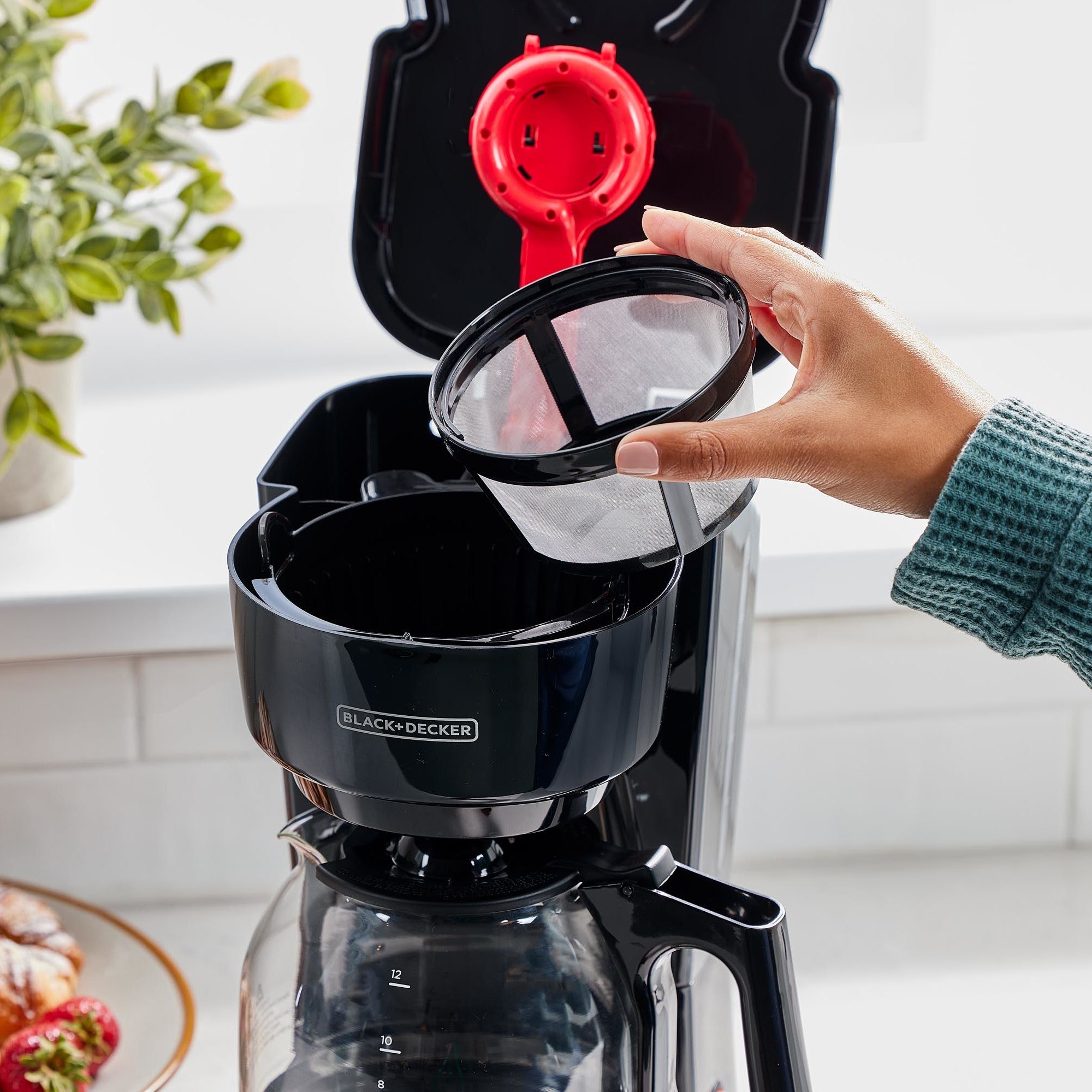 Person using a Black+Decker coffee maker with a red filter on a kitchen counter.